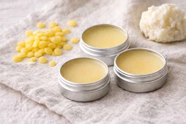 Drei fertige natürliche Lippenbalsam-Tiegel mit Sheabutter und Bienenwachspastillen drumherum