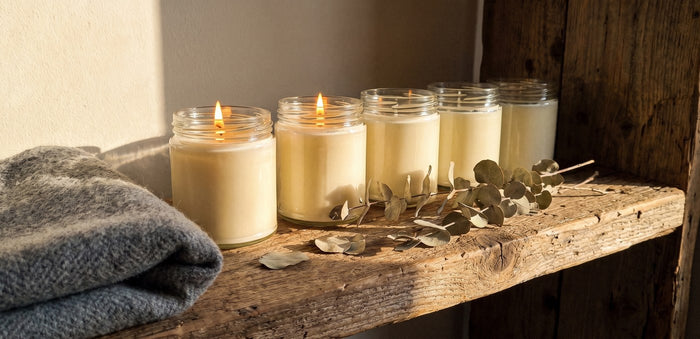 Fünf fertige Sojakerzen im Glas auf einem Holzregal, zwei davon brennen